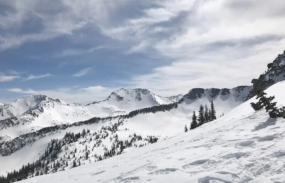 Snow-covered mountain peaks under partly cloudy sky with scattered evergreens