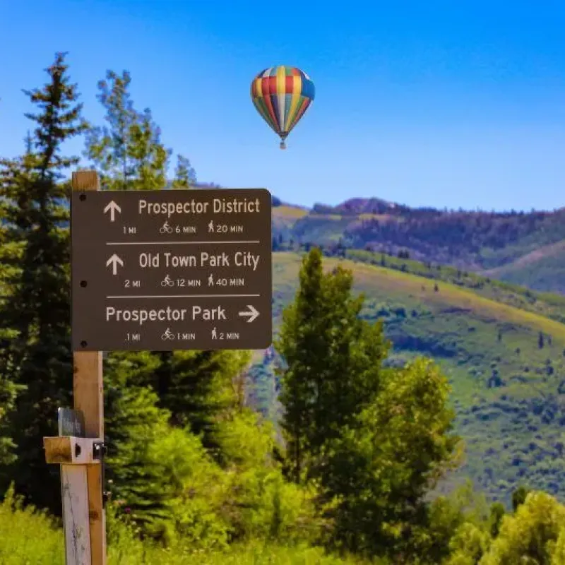 Trail signpost for Park City paths with hot air balloon over green hills