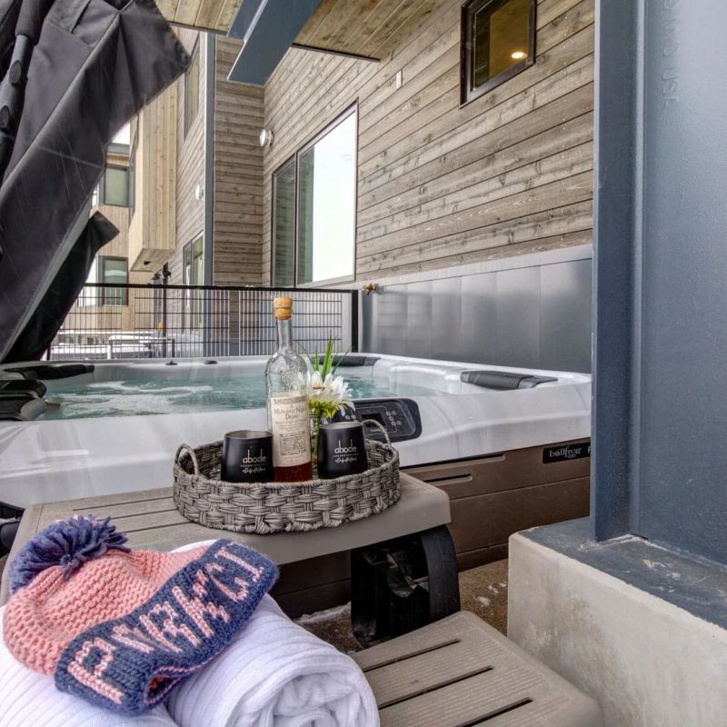 Snow-dusted private hot tub on a deck with Park City branded mugs and winter beanie towel