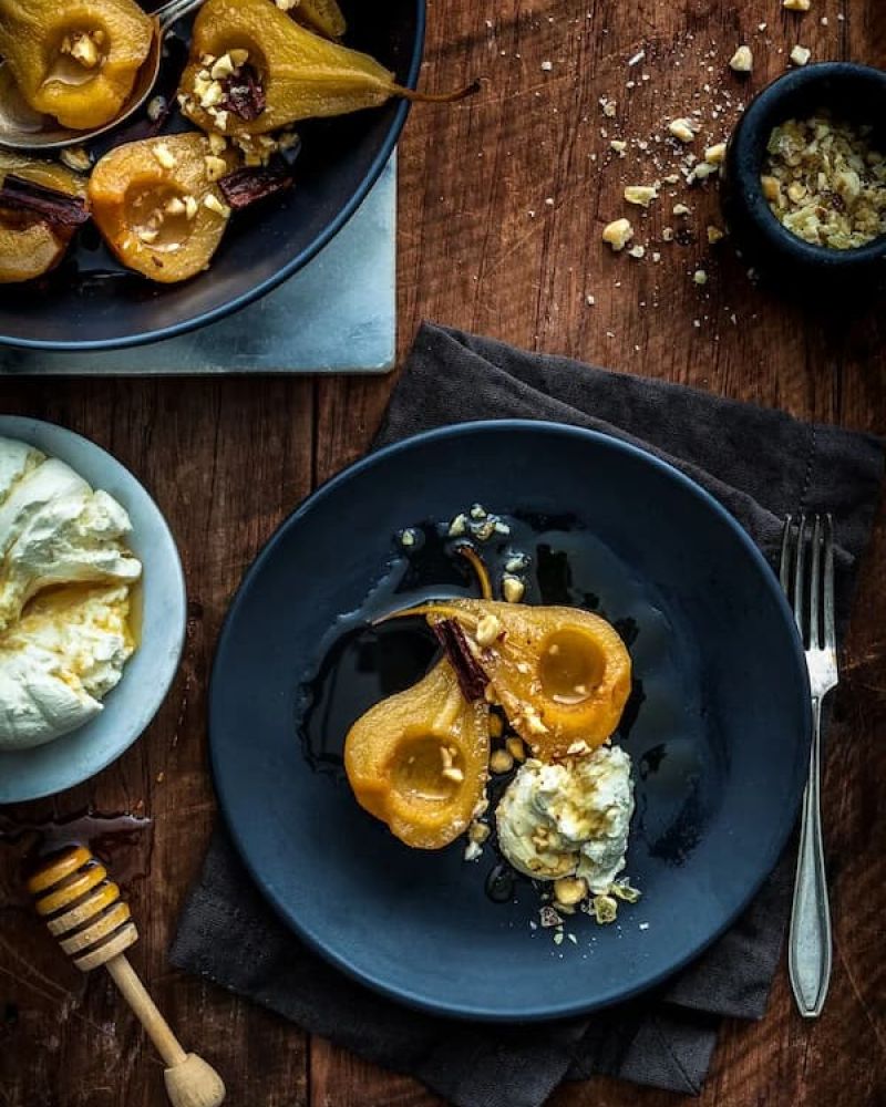 Poached pears with cinnamon, walnuts, and cream on a dark plate