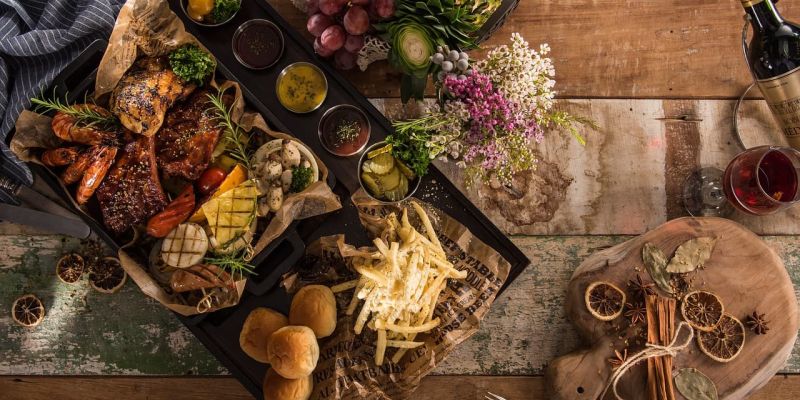 Overhead spread of grilled meats, fries, fruit and wine on a wood table