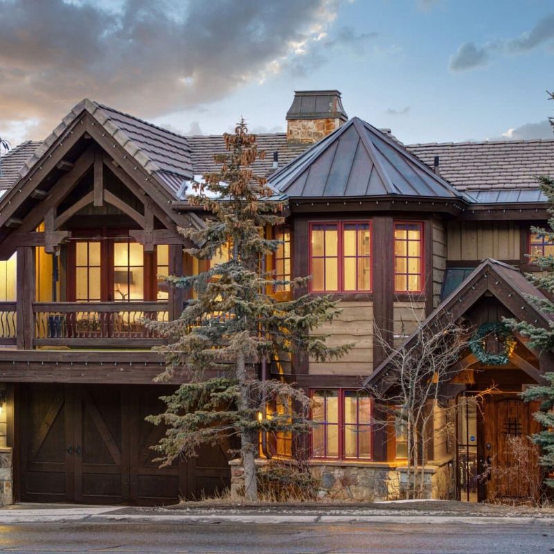 Timber-and-stone mountain home exterior at dusk with lit windows and evergreens