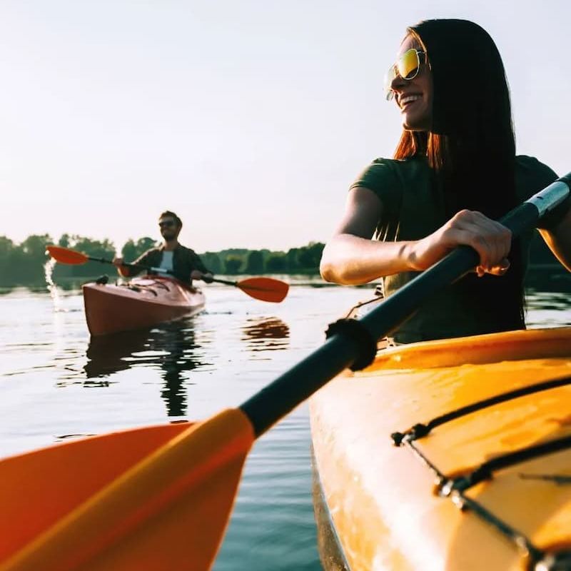 Two kayakers paddling on calm water at sunset