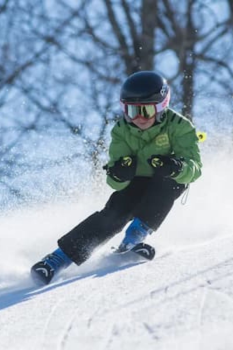 Young skier in green jacket carving a turn down a snowy slope