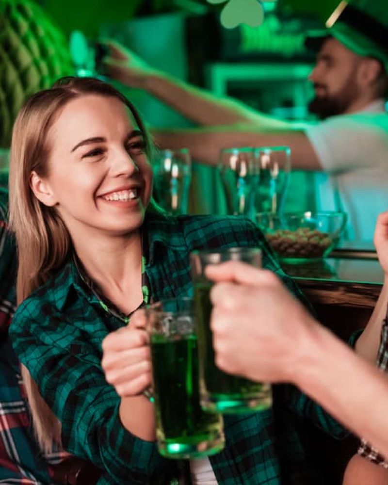 Two friends in green attire toasting pints of green beer at a St. Patrick's Day pub