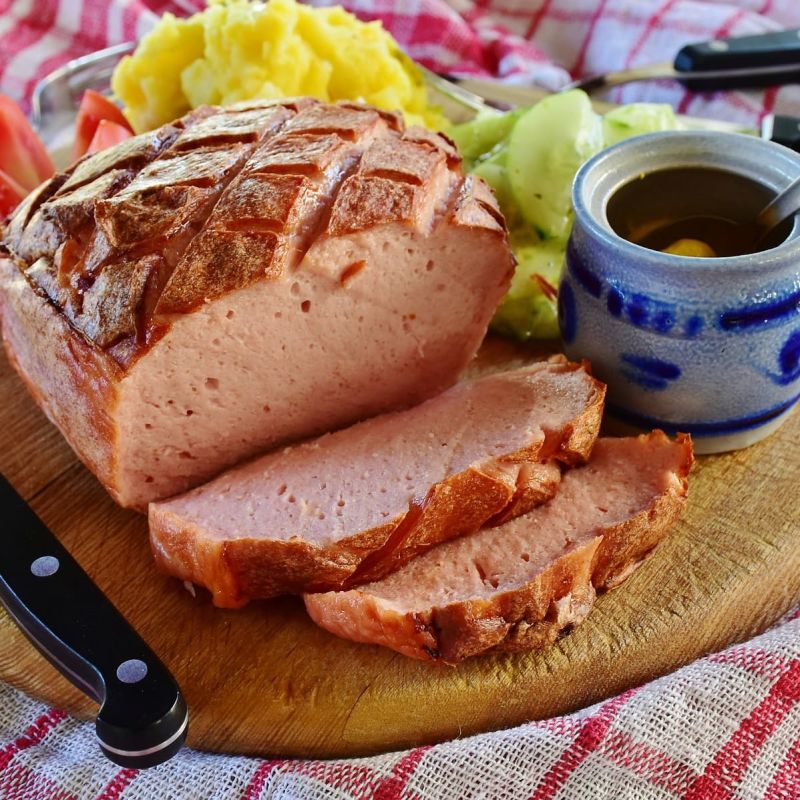 Sliced meatloaf on a wooden board with mustard and potatoes