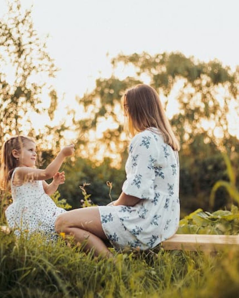 Mother and young daughter sitting on a bench in a sunlit meadow at golden hour