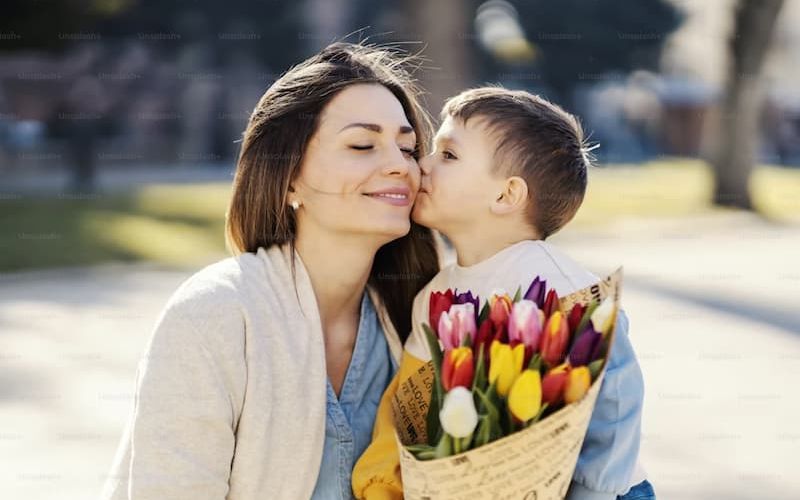 Young boy kissing his smiling mother's cheek while holding a tulip bouquet