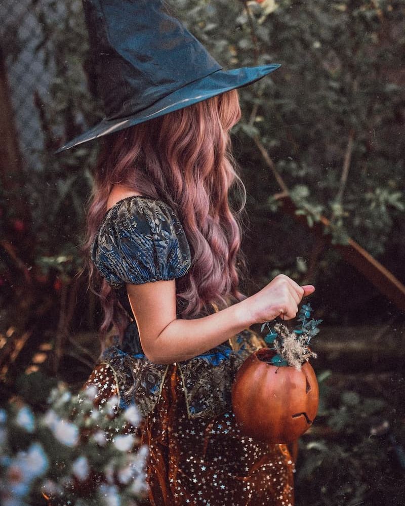 Person in witch hat and starry costume holding a pumpkin pail outdoors