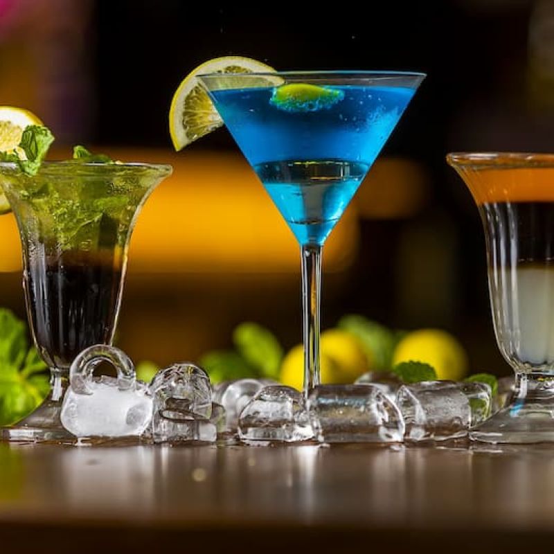 Three garnished cocktails on a bar with mint and citrus