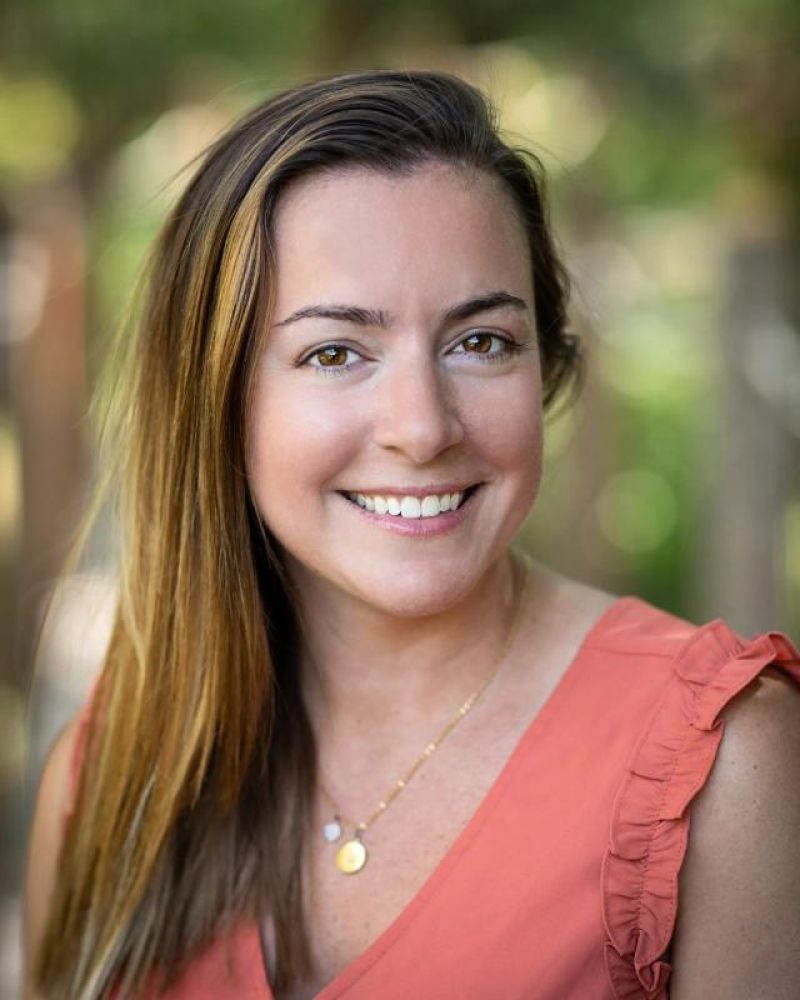 Headshot of a smiling woman in a coral sleeveless top