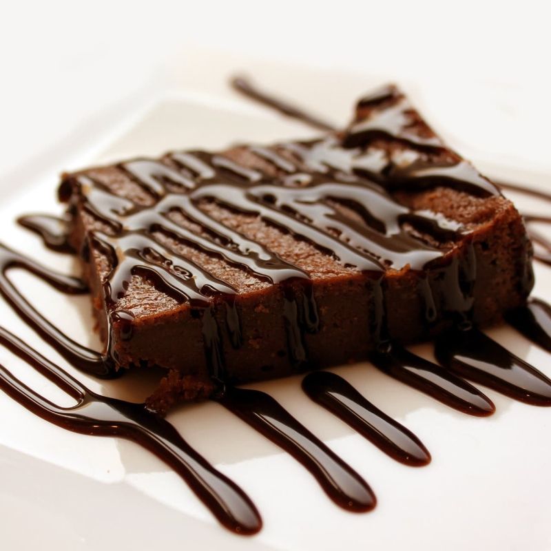 Slice of chocolate cake drizzled with chocolate sauce on a white plate