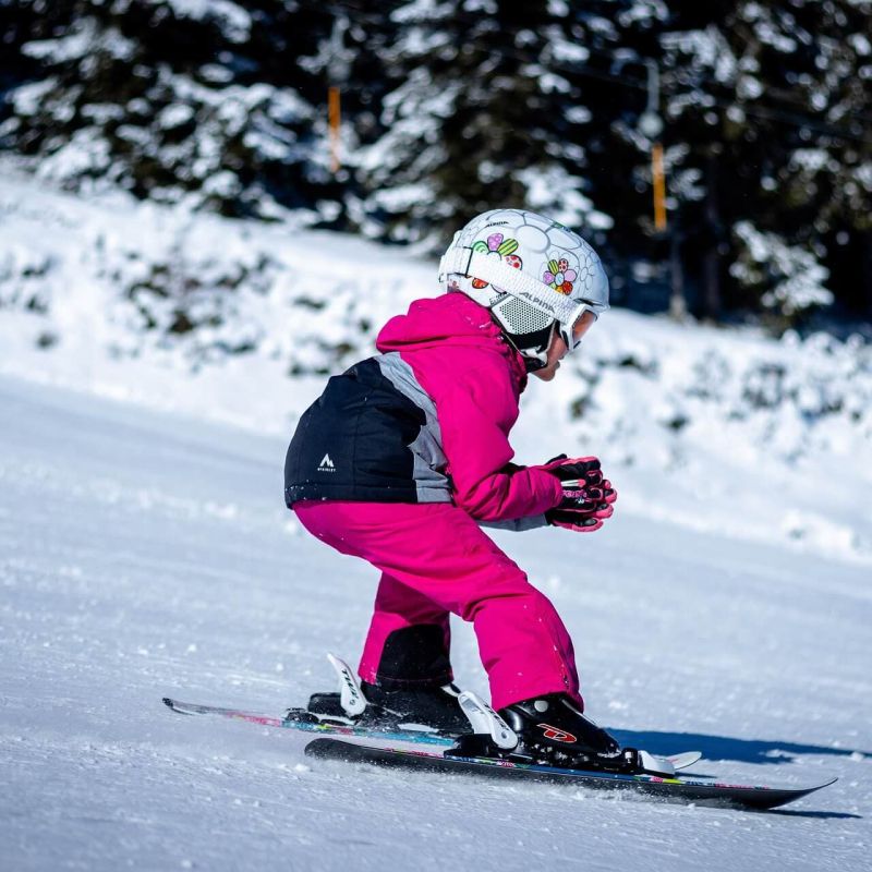 Child in pink ski gear carving a turn down a groomed run