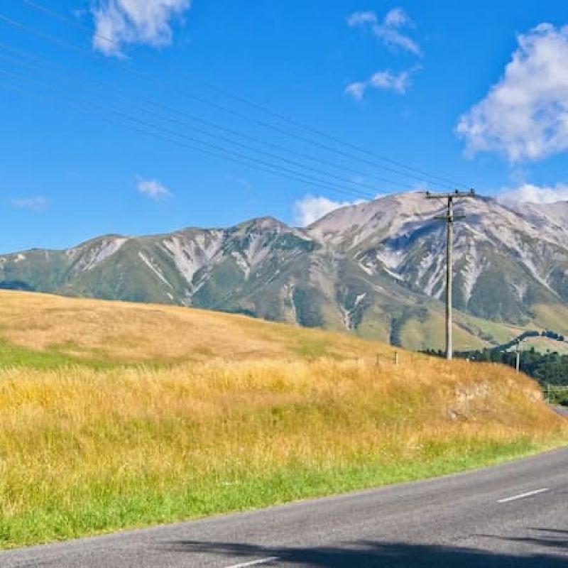 Empty country road curving past golden grassland toward a mountain ridge