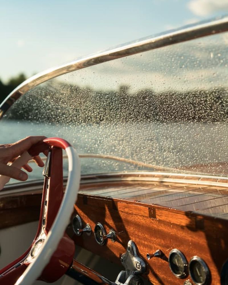 Hand on the steering wheel of a wooden classic speedboat at golden hour