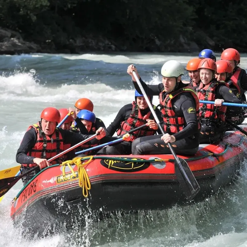 Group of rafters in a red raft paddling through whitewater rapids