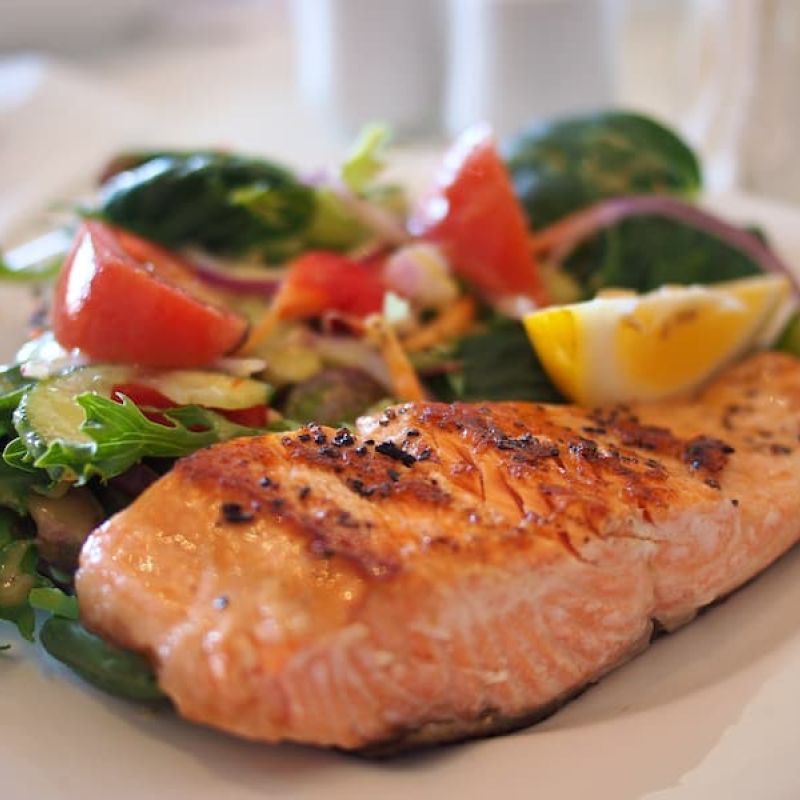 Grilled salmon fillet with mixed greens and lemon wedge