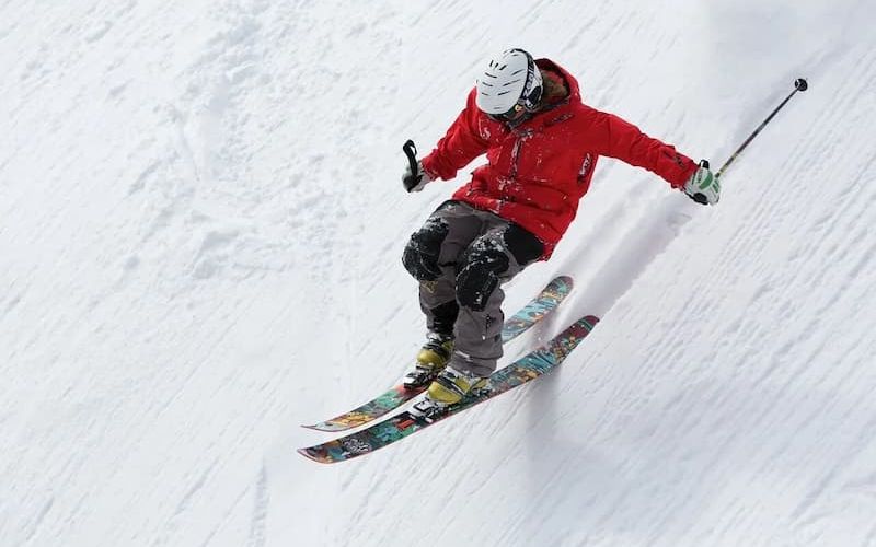Skier in a red jacket carving down a steep groomed run