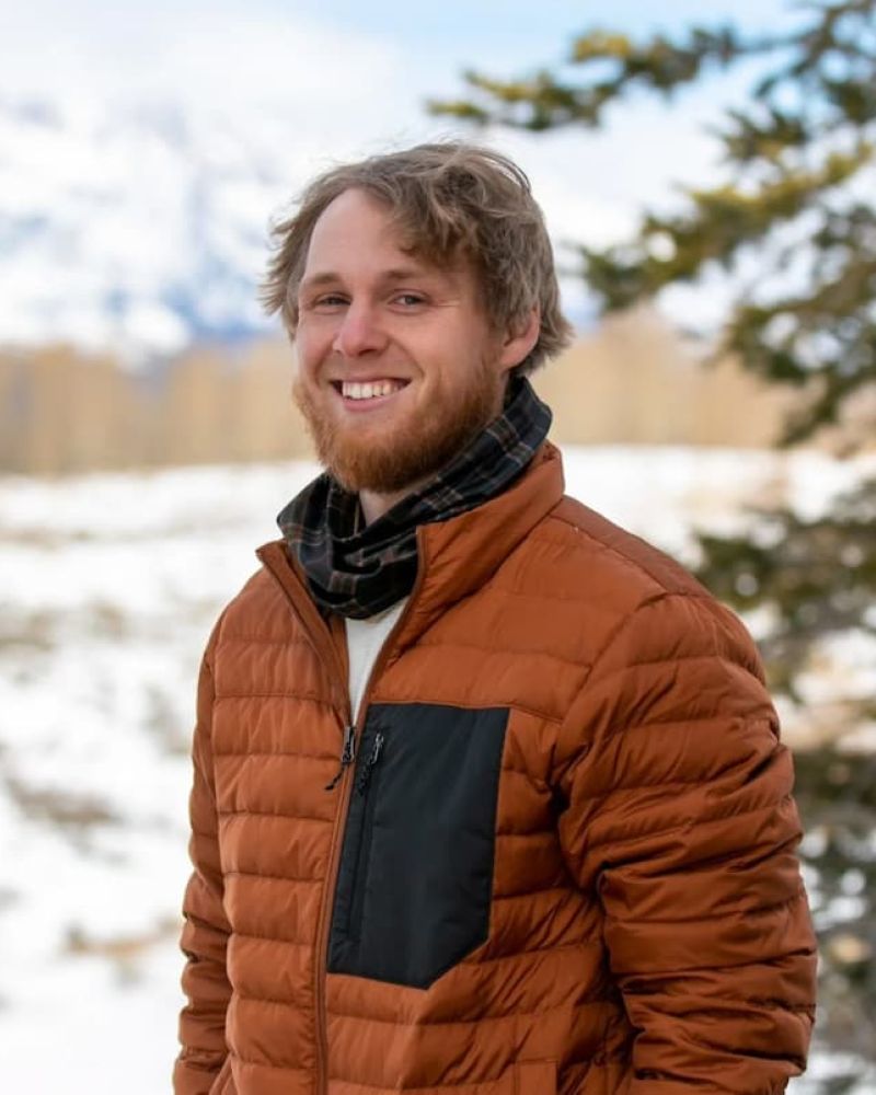 Smiling young man in orange puffer jacket and flannel scarf outdoors in winter