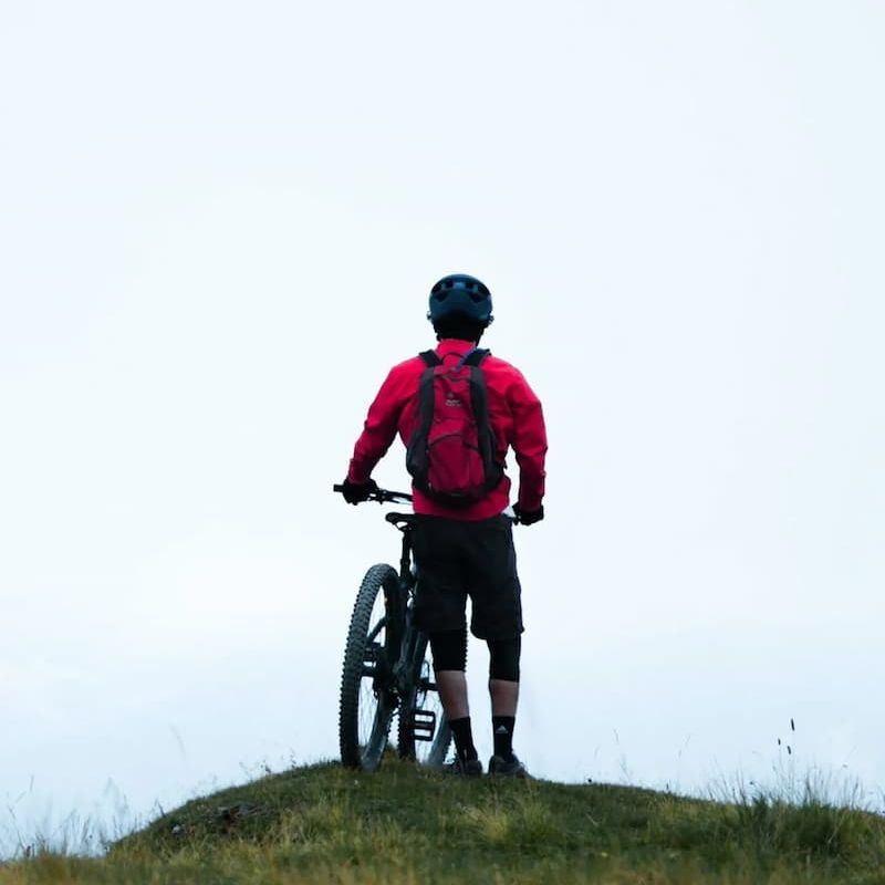 Mountain biker in red jacket pausing atop a grassy hill