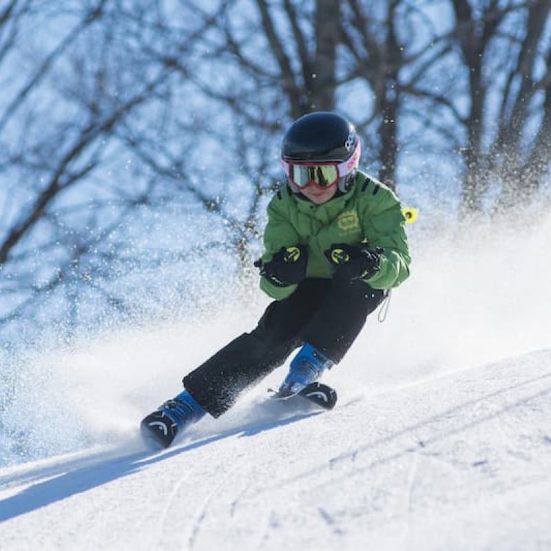 Young skier in green jacket carving a turn through fresh snow