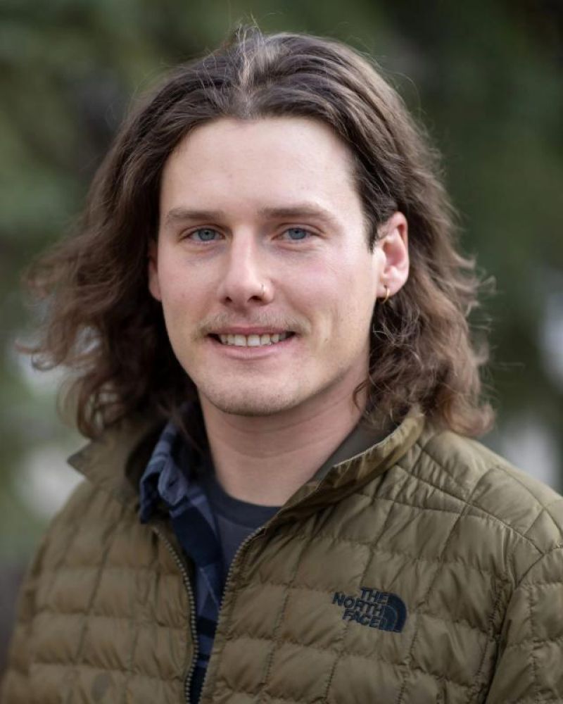 Headshot of a smiling man with long hair in a North Face jacket