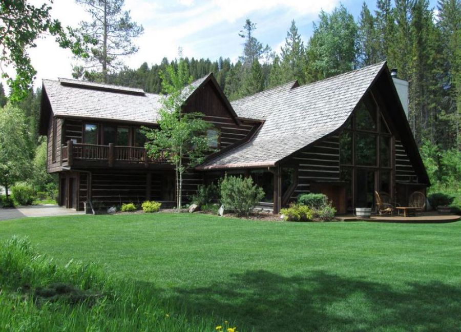 Log cabin with steep cedar-shingle roof set on a green lawn