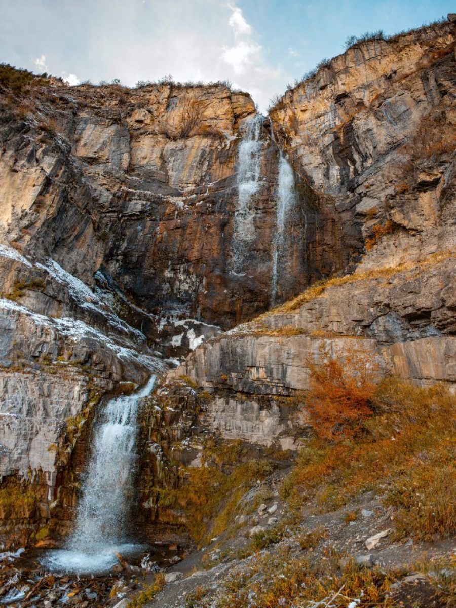 Tall waterfall cascading down red rock cliffs with autumn foliage below