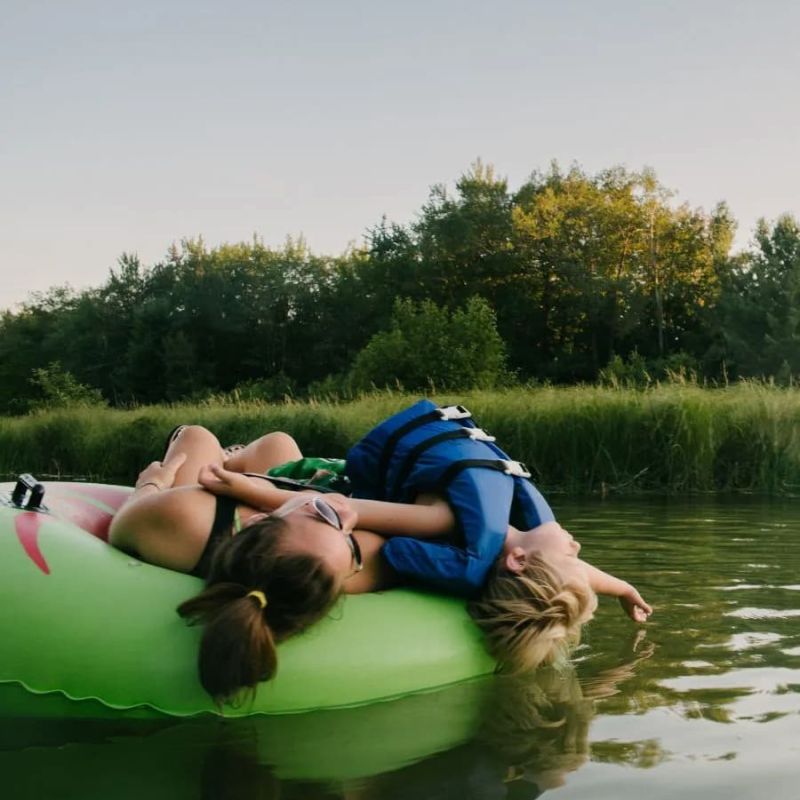 Two friends lounging on a green inflatable tube on a quiet river