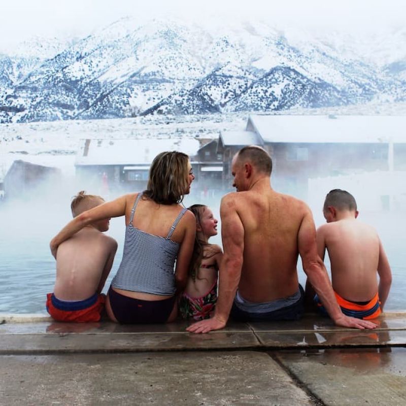 Family seated on the edge of a steaming hot spring with snowy mountains behind