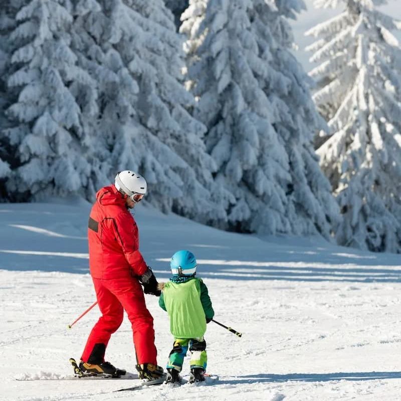 Ski instructor guiding a young child on a snowy beginner slope