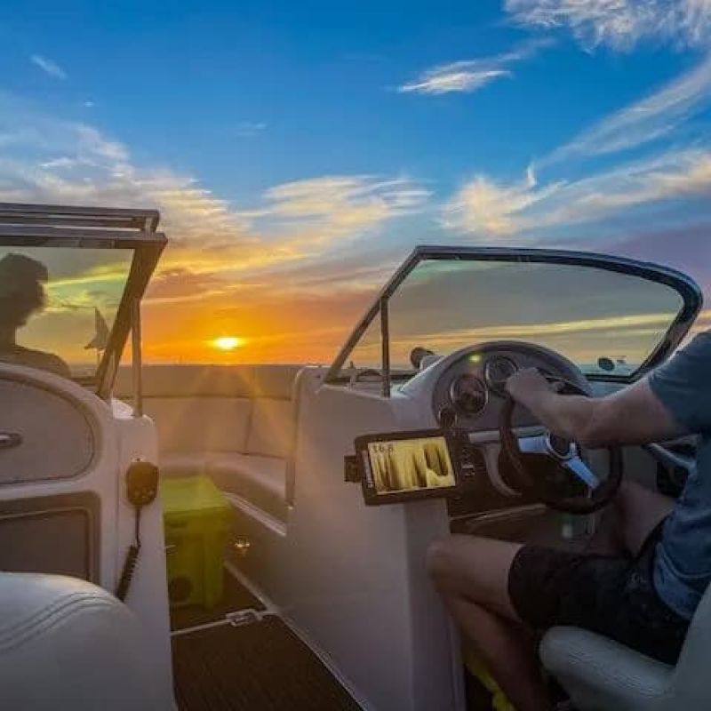 Boater steering a powerboat into the sunset on a calm lake