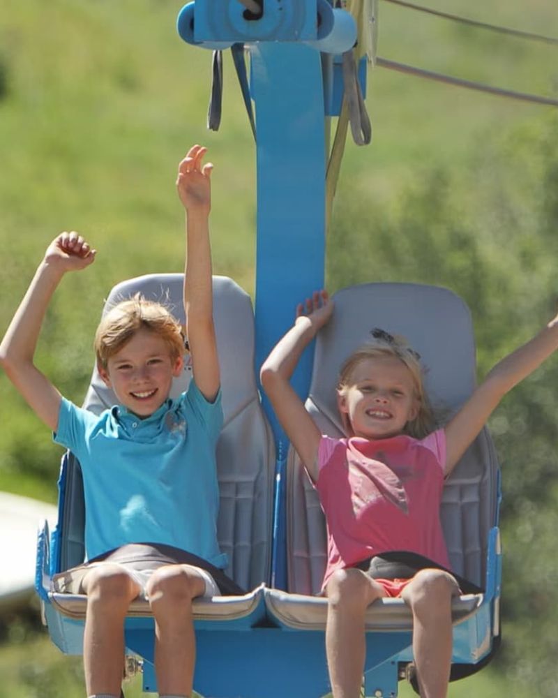 Two children riding a chairlift with arms raised in the air