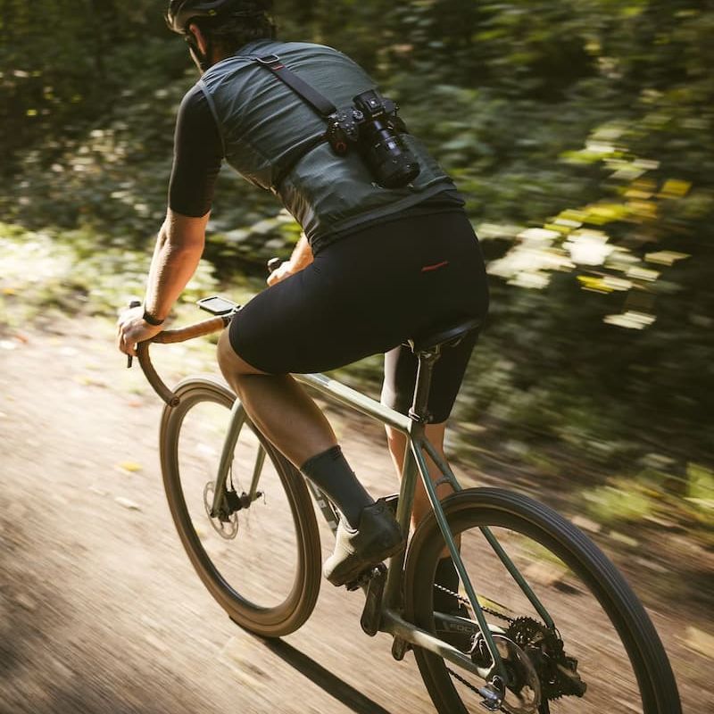 Gravel cyclist with shoulder-strap camera riding fast through forest