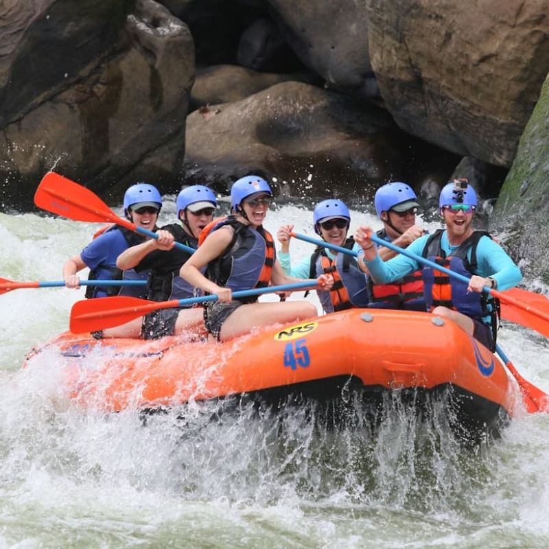 Group whitewater rafting through churning rapids in an orange raft