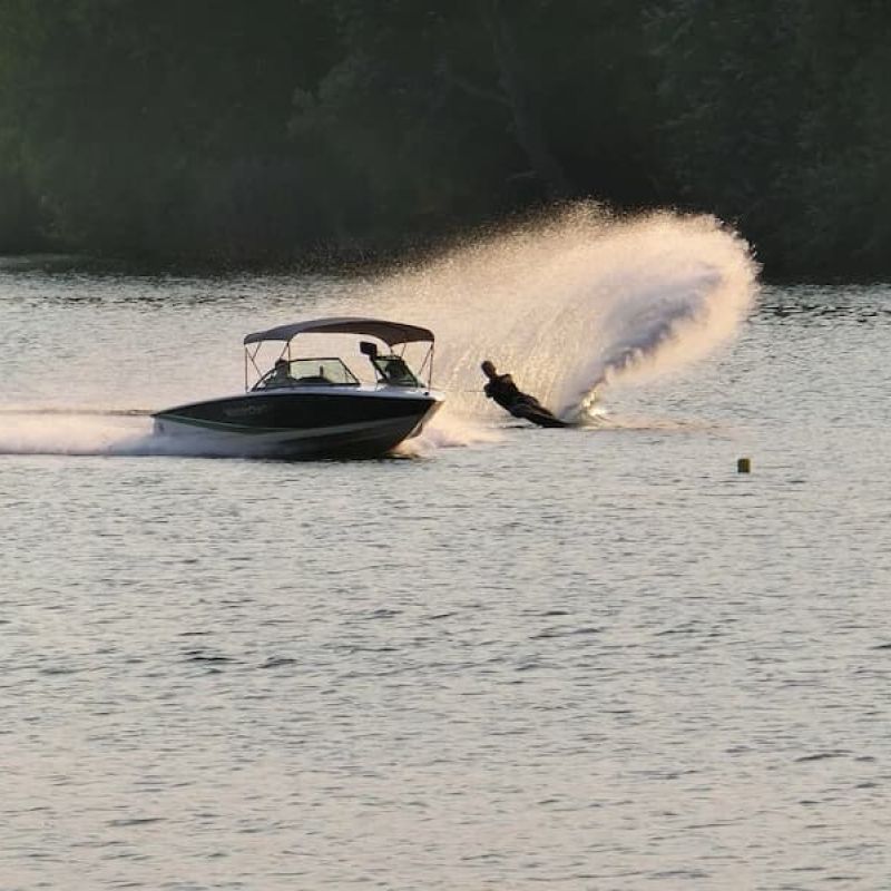 Waterskier carving a spray behind a ski boat on calm water