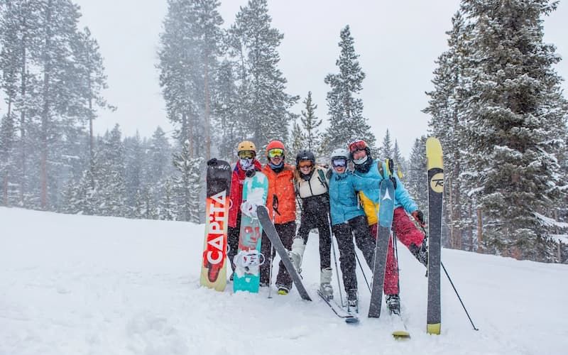 Five skiers and snowboarders posing with their gear on a snowy slope