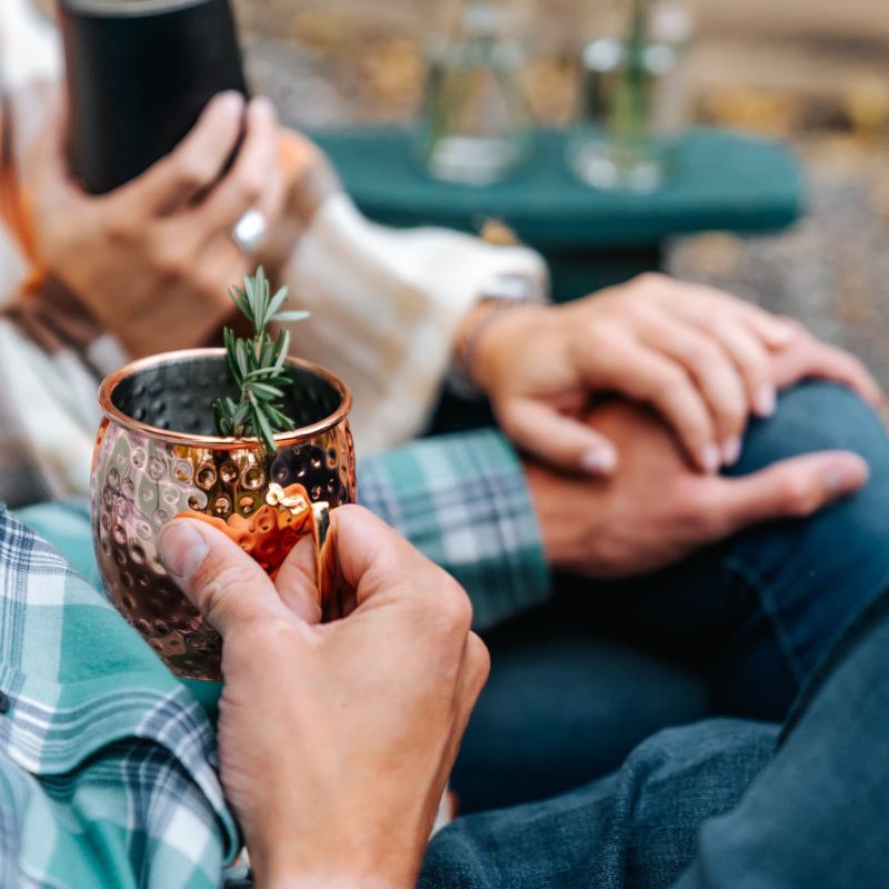 Close-up of hands holding a copper mug garnished with rosemary outdoors