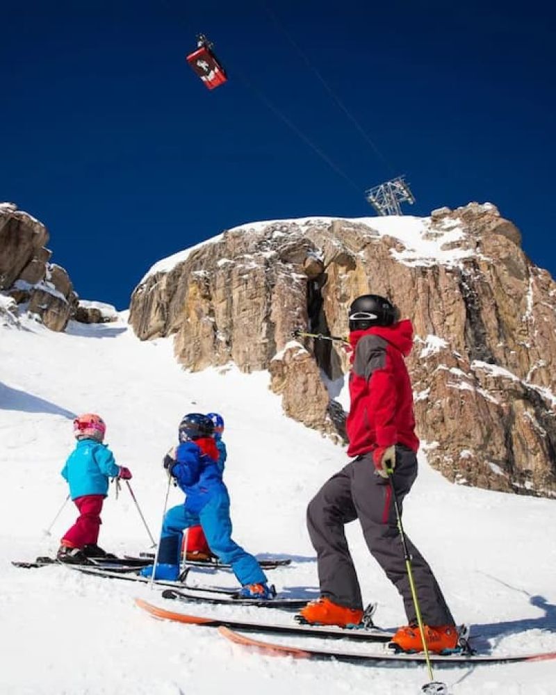 Skiers and tram cabin near a rocky peak at Jackson Hole