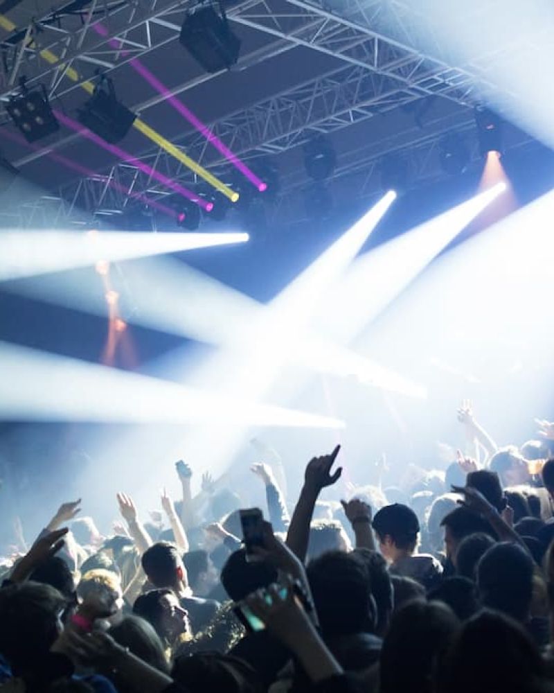 Indoor concert crowd with stage lights and lasers cutting through fog