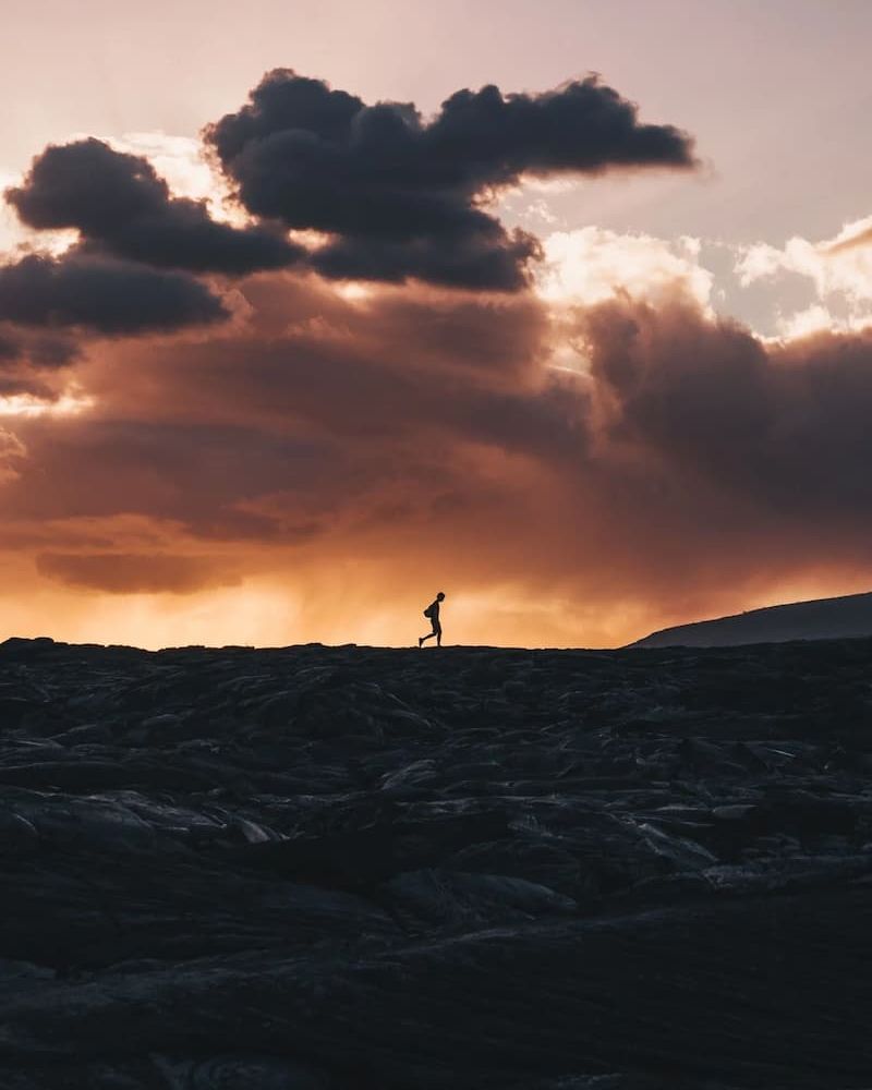Hiker silhouetted on a rocky ridge under a glowing sunset sky