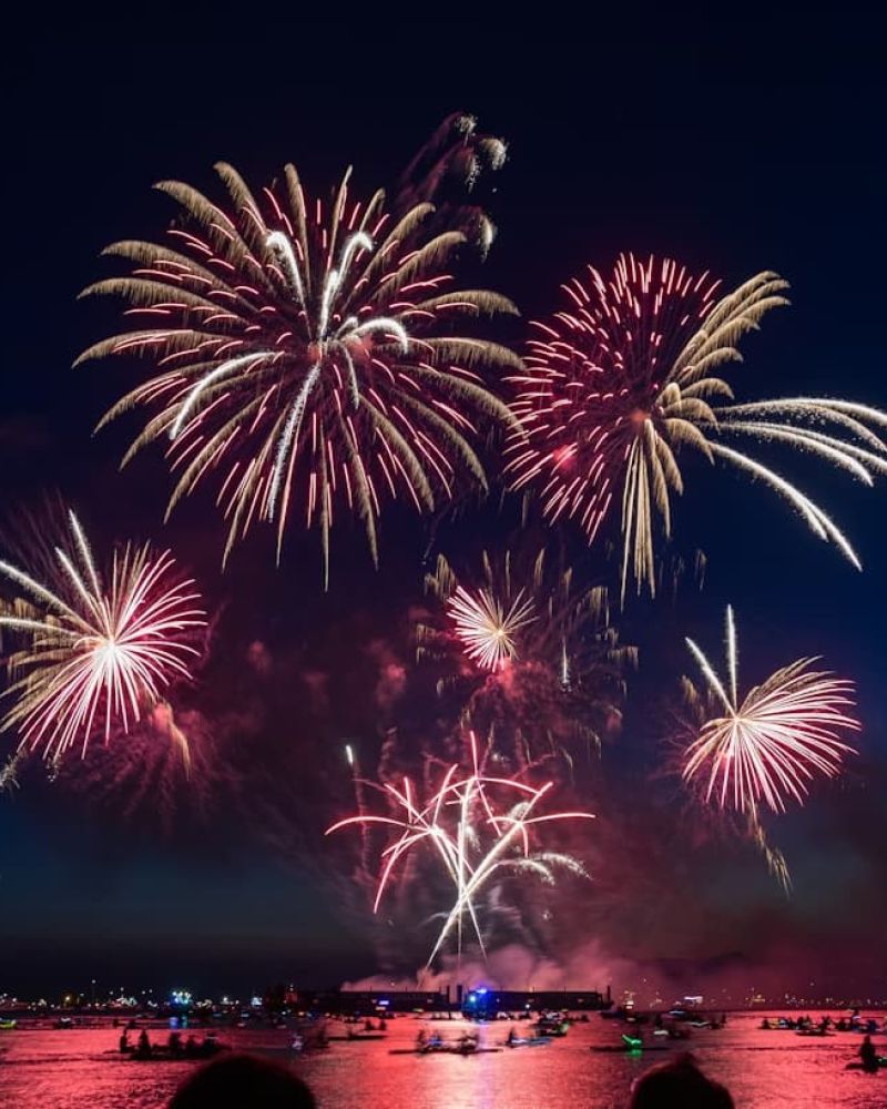 Red and gold fireworks exploding above boats on a lake at night