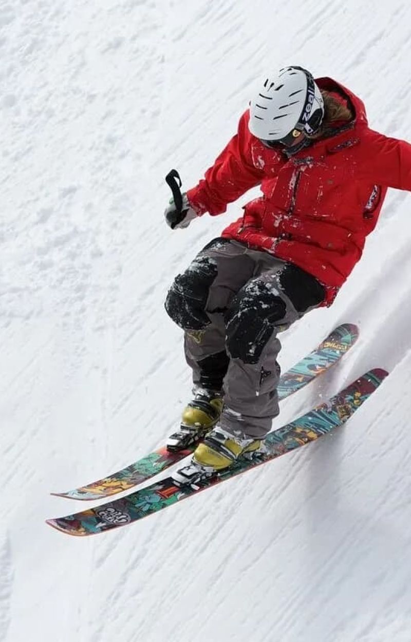 Skier in red jacket carving turns down a snowy slope