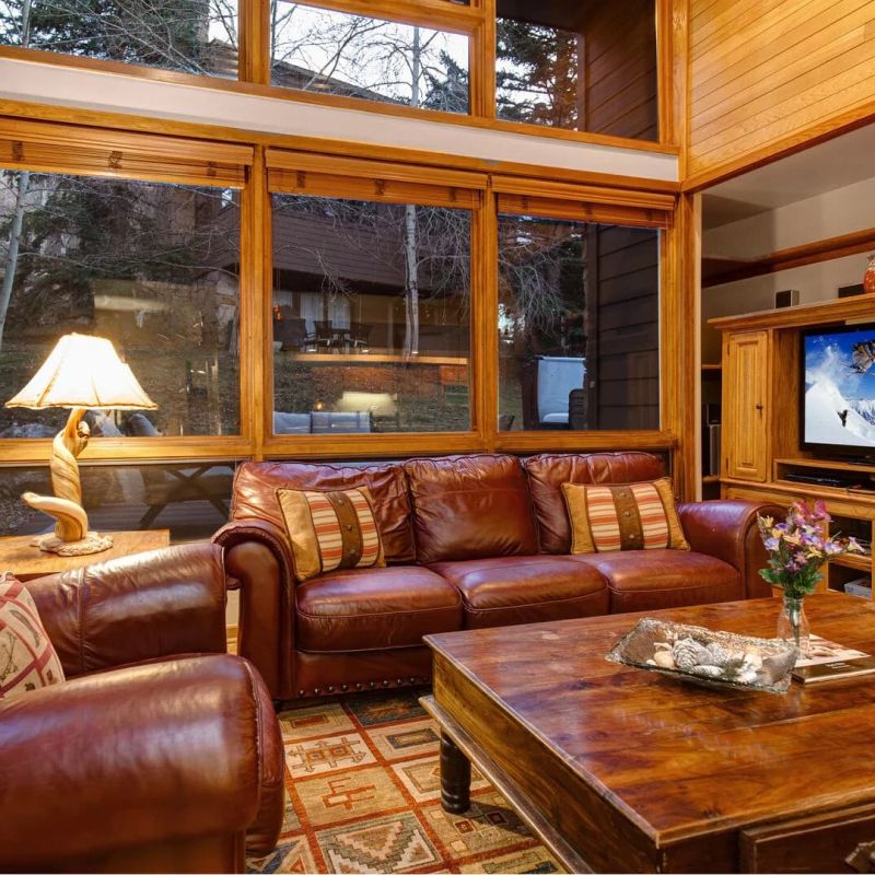Wood-paneled den with leather sofas, large windows, and mounted TV