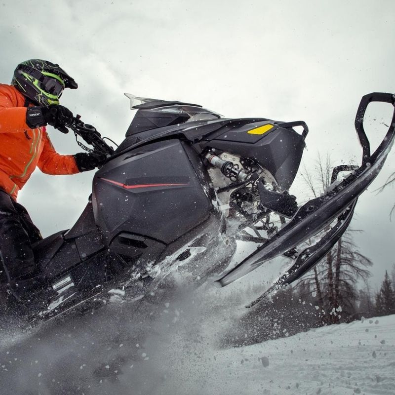 Snowmobiler in orange jacket carving through powder kicking up snow spray