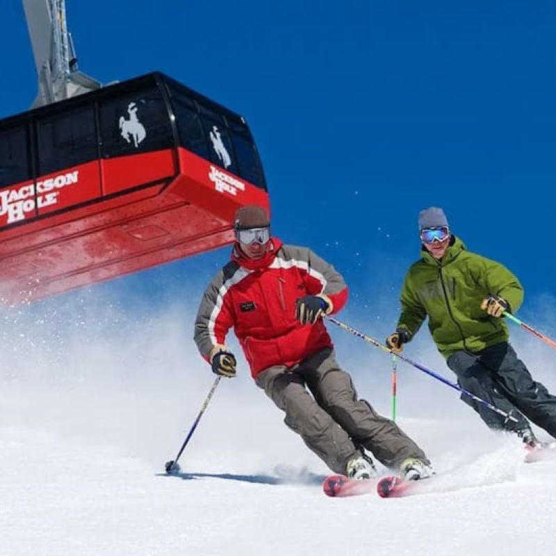 Two skiers carving down a slope below the Jackson Hole aerial tram