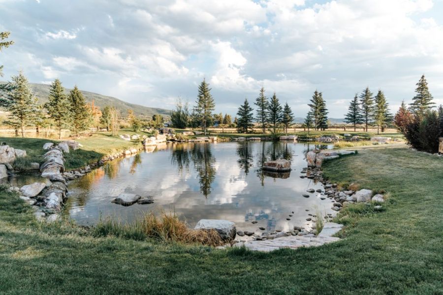 Reflective pond surrounded by evergreens and rolling hills at twilight