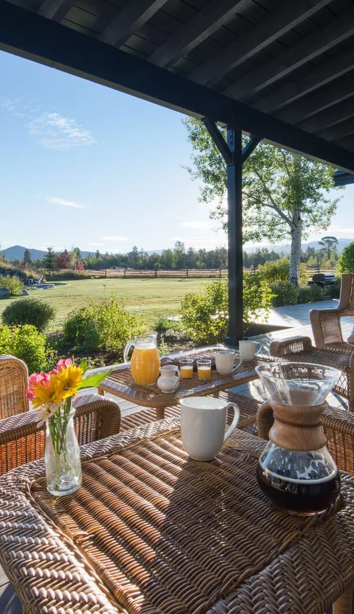 Covered patio table set with coffee and juice overlooking a pasture and mountains