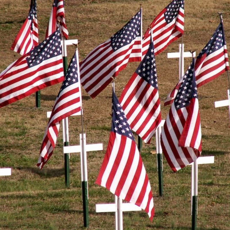 Memorial display of American flags and white crosses on a grass lawn
