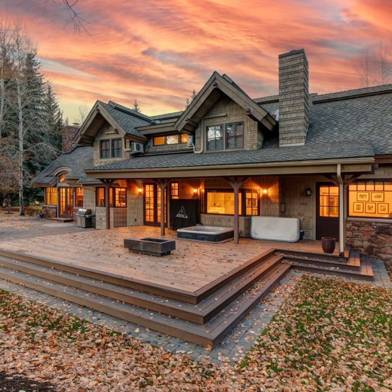 Craftsman home exterior with stone chimney and back deck at sunset